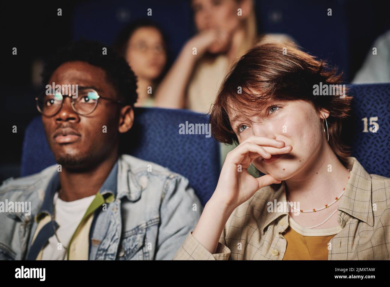 Medium close-up portrait of young Black mana and Caucasian woman spending evening together crying while watching tragedy movie at cinema Stock Photo