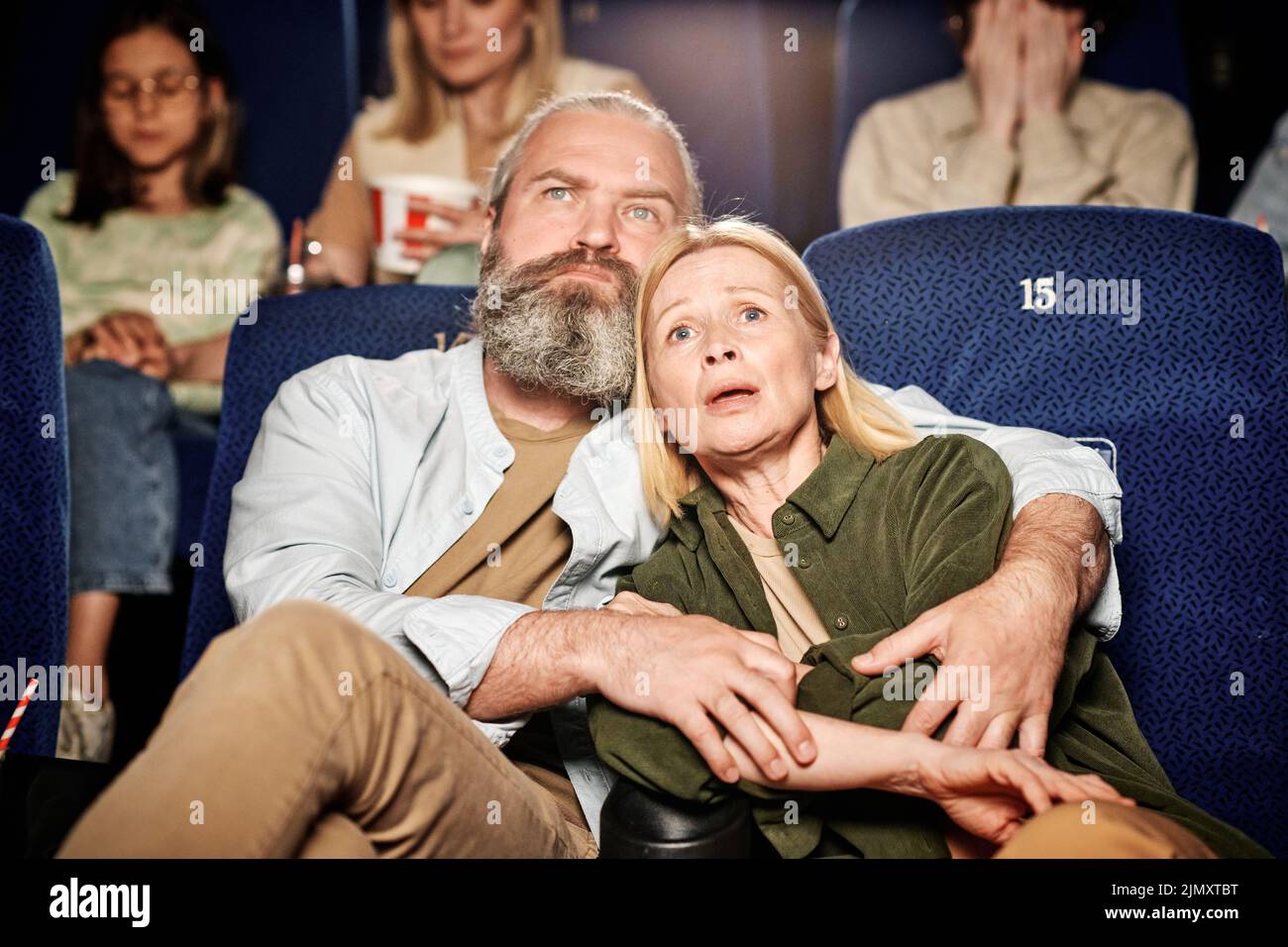 Portrait of mature adult Caucasian man hugging his wife watching tragedy movie together at cinema Stock Photo