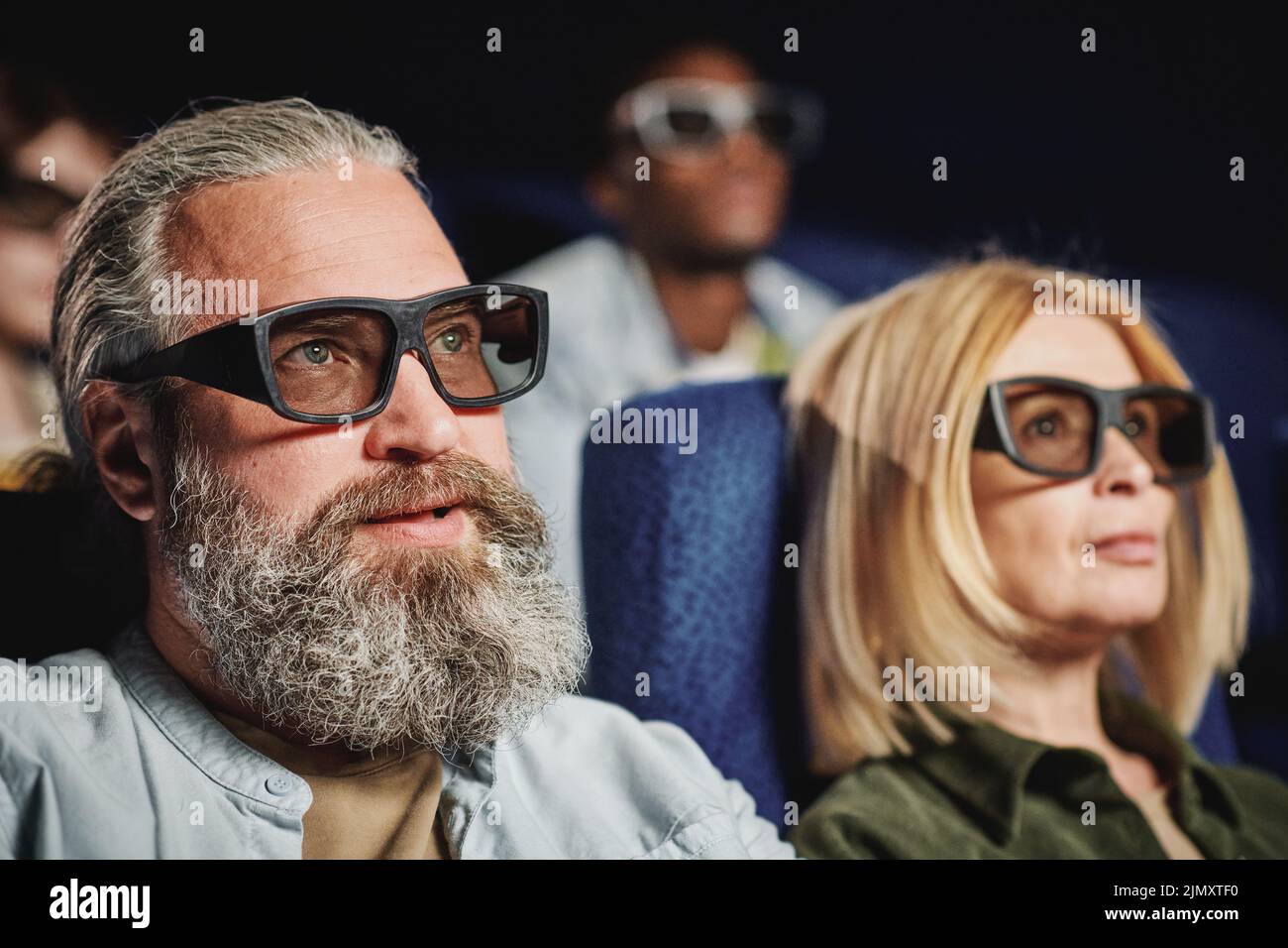 Selective focus shot of of handsome mature man with beard on face wearing 3D eyeglasses watching movie in cinema Stock Photo