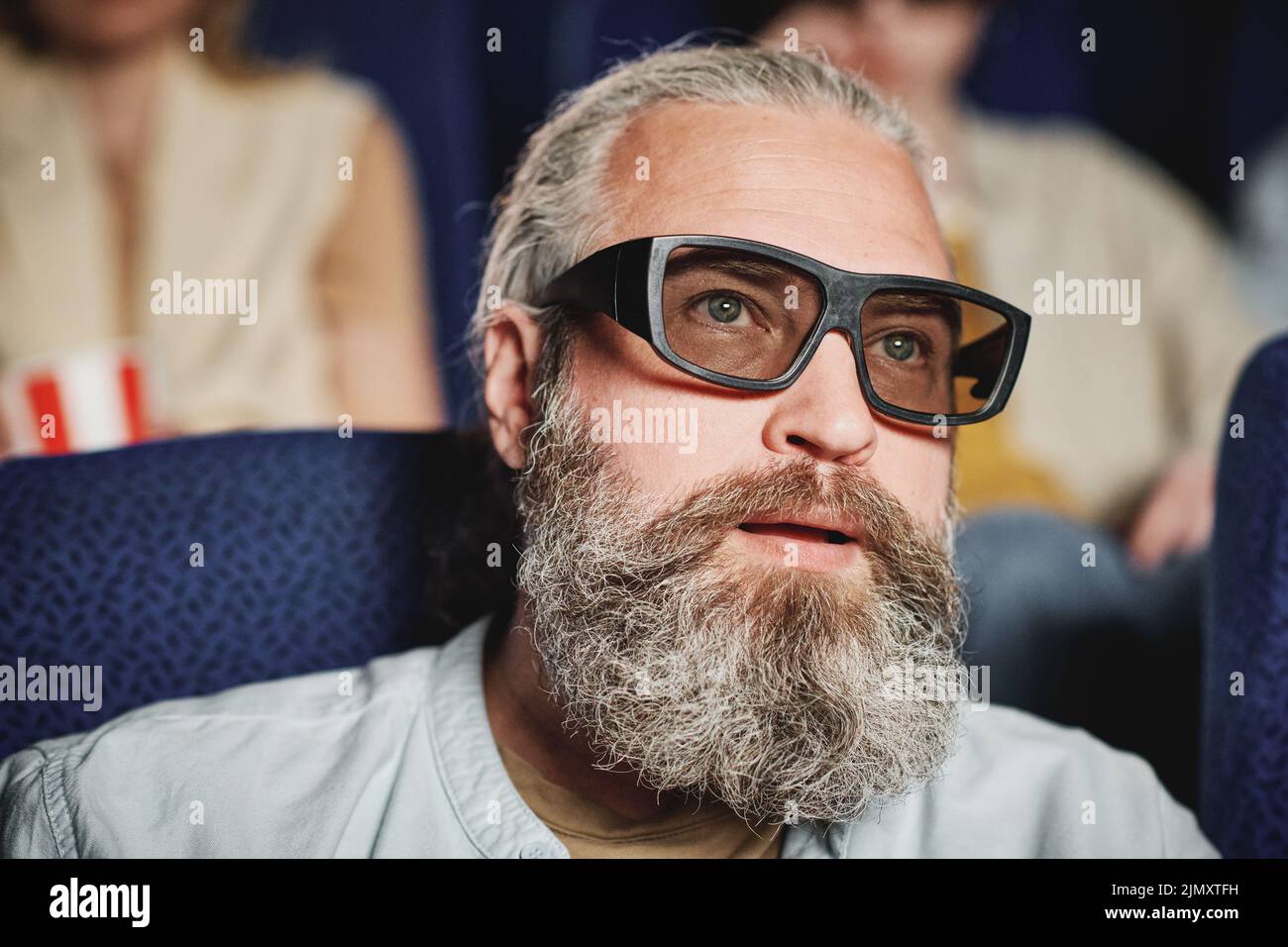 Close-up portrait of mature Caucasian man with beard on face wearing polarized 3D glasses watching movie in cinema Stock Photo