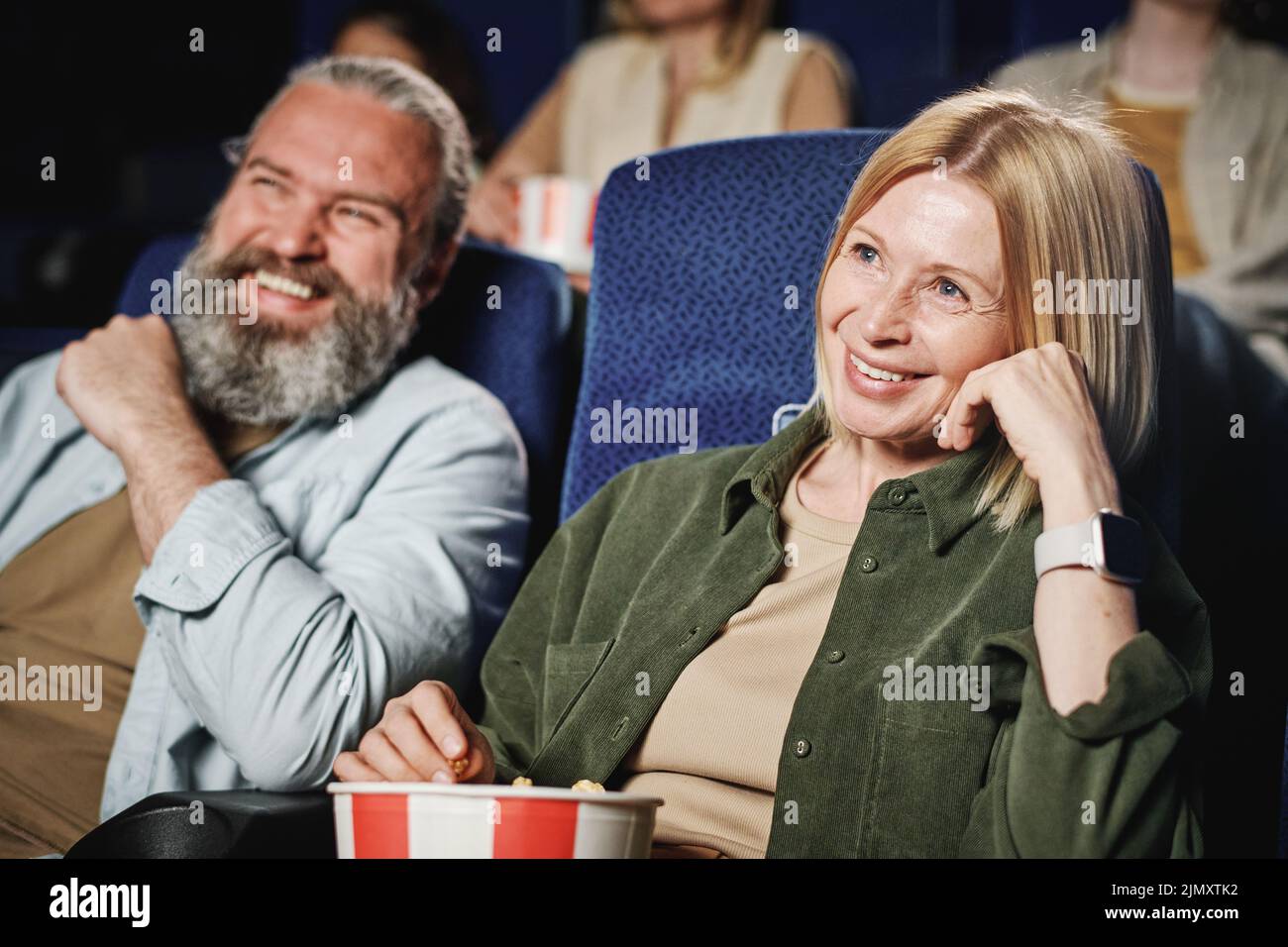 Selective focus of mature Caucasian woman and her husband spending time together watching interesting movie at cinema Stock Photo