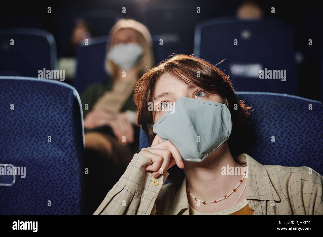 Unrecognizable young Caucasian woman wearing protective mask watching movie at cinema, quarantine concept Stock Photo