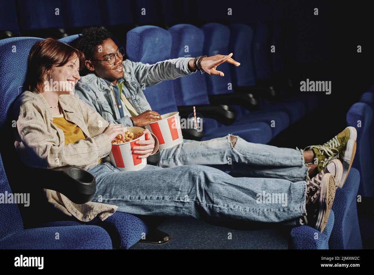 Young gen Z African American man and Caucasian woman in love wearing casual clothes enjoying watching action movie at cinema Stock Photo