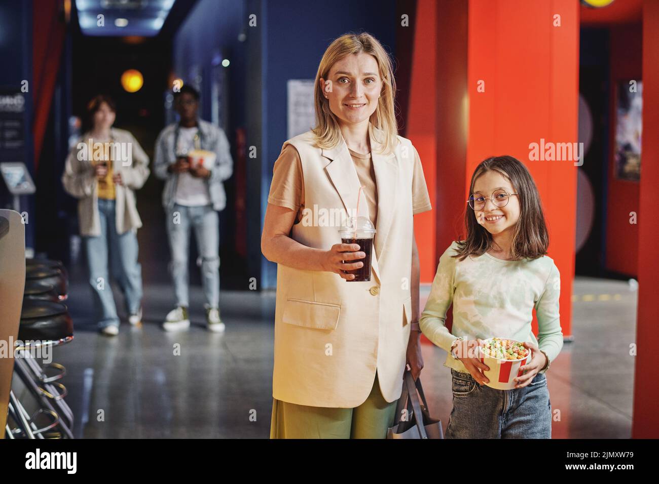 Portrait of stylish Caucasian mother and preteen daughter holding cup of cola and bucket of popcorn going to watch movie at cinema Stock Photo