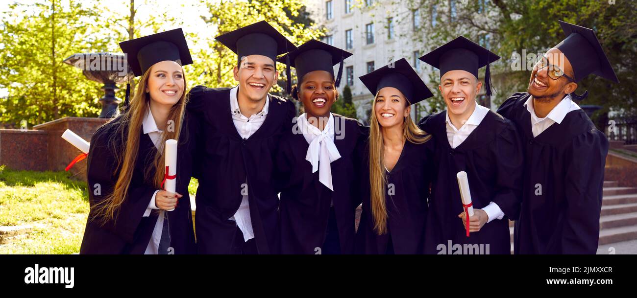 Banner with group portrait of happy multiracial university graduates in caps and gowns Stock Photo