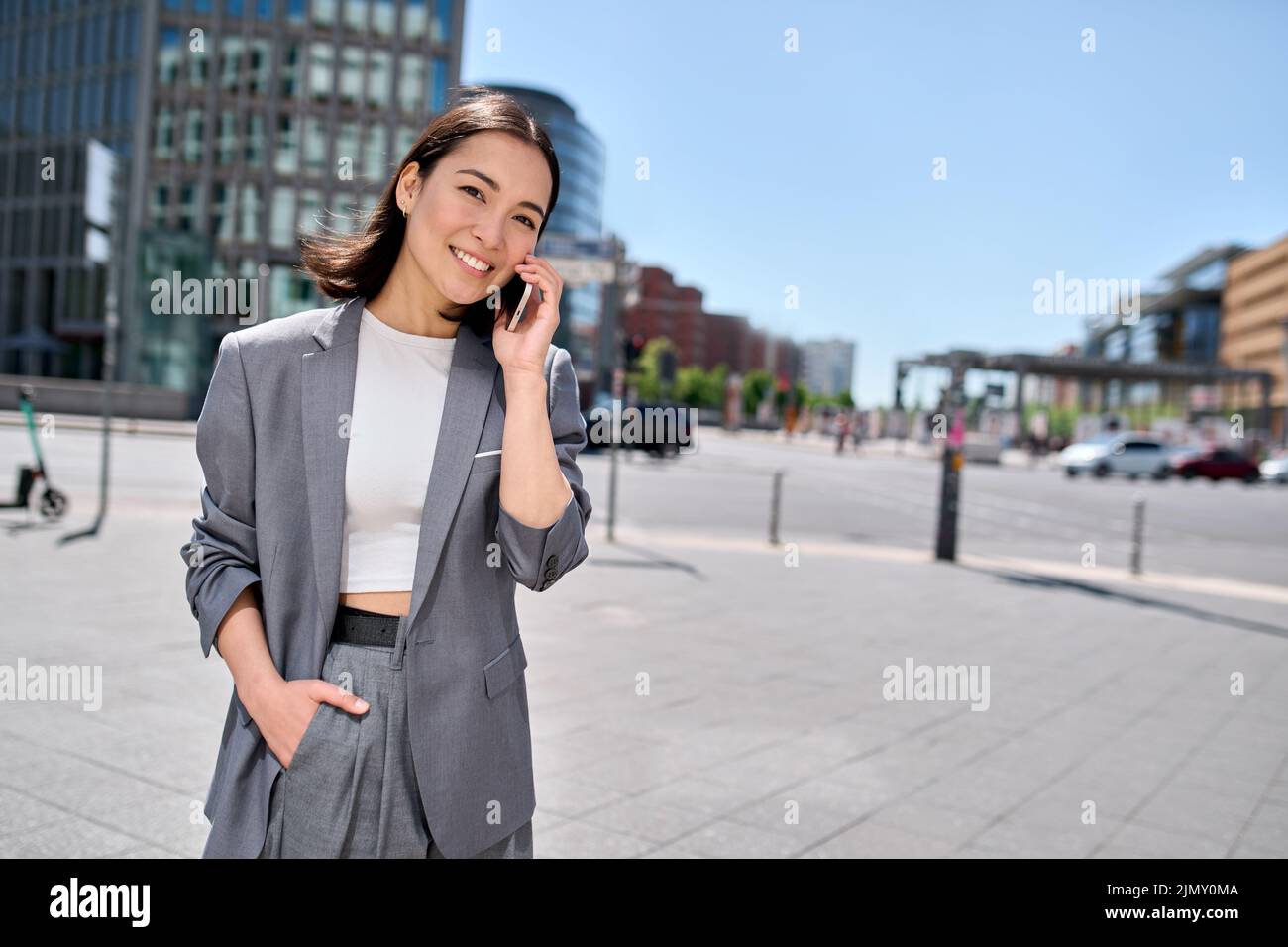 Young happy Asian business woman entrepreneur talking on phone on city ...
