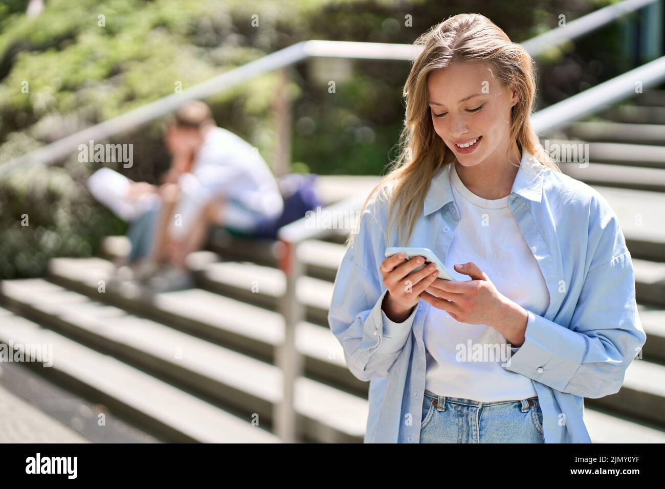 Young smiling woman university student using cellphone standing outdoors. Stock Photo