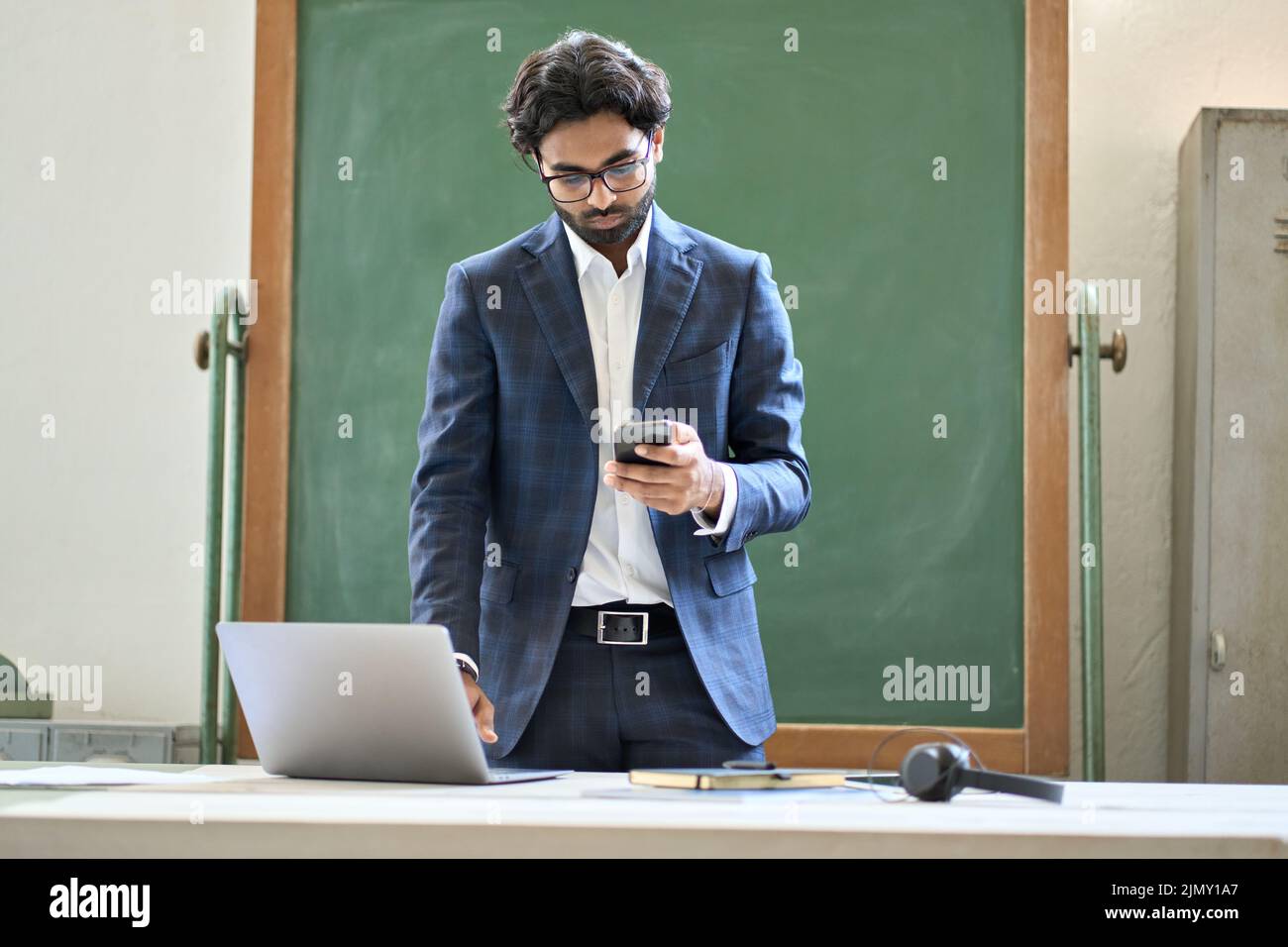 Young indian business man using phone working on laptop in office. Stock Photo