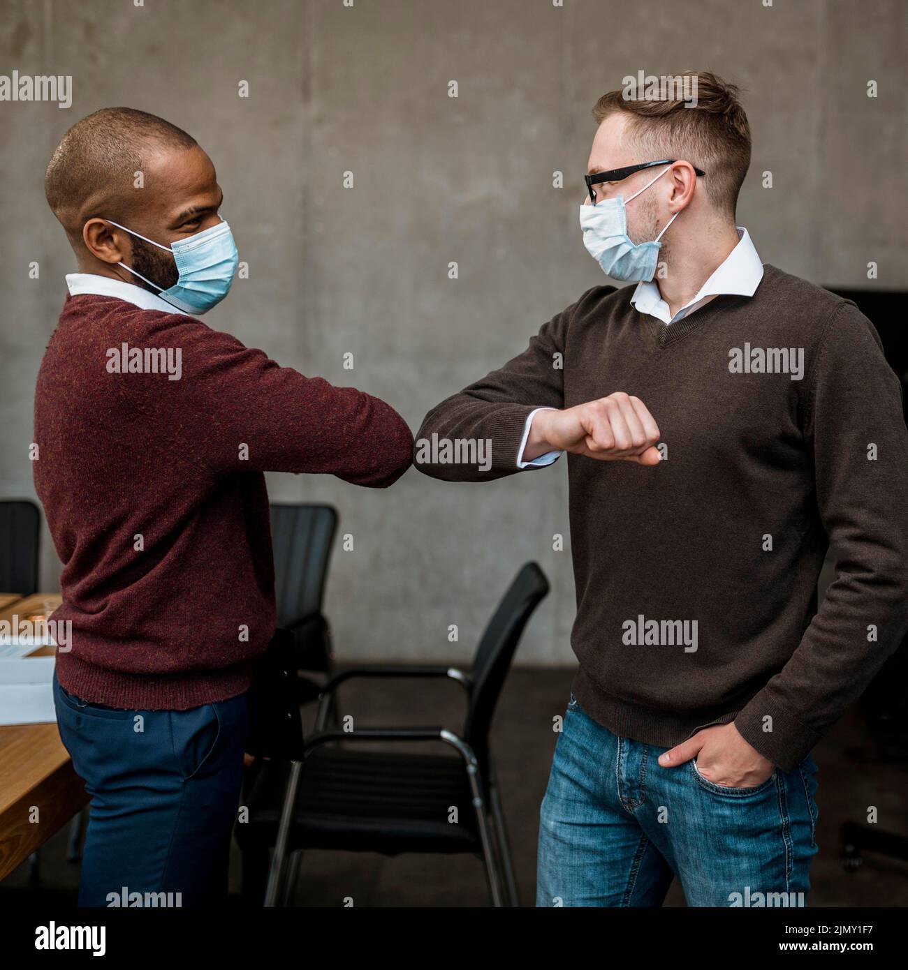Side view men elbow saluting each other during meeting wearing medical masks Stock Photo