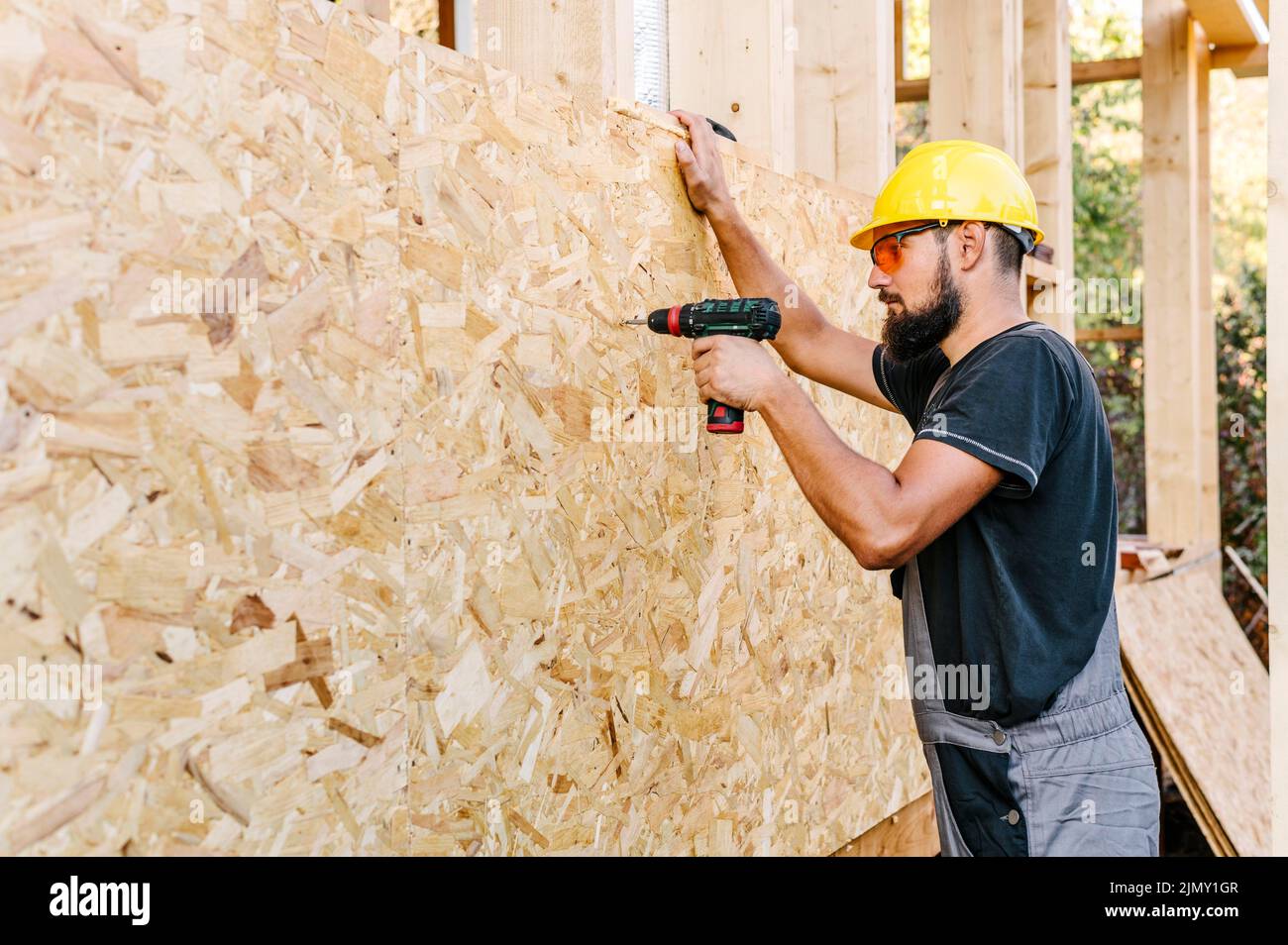 Side view construction worker drilling plywood with copy space Stock