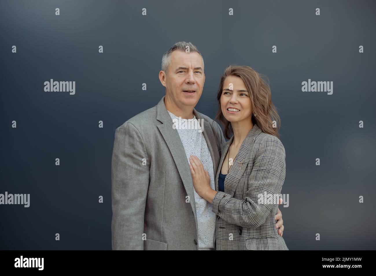 Happy young loving woman and handsome aged gray haired partner gently embracing, gray background. Romantic relations of beautiful couple. Happy family Stock Photo