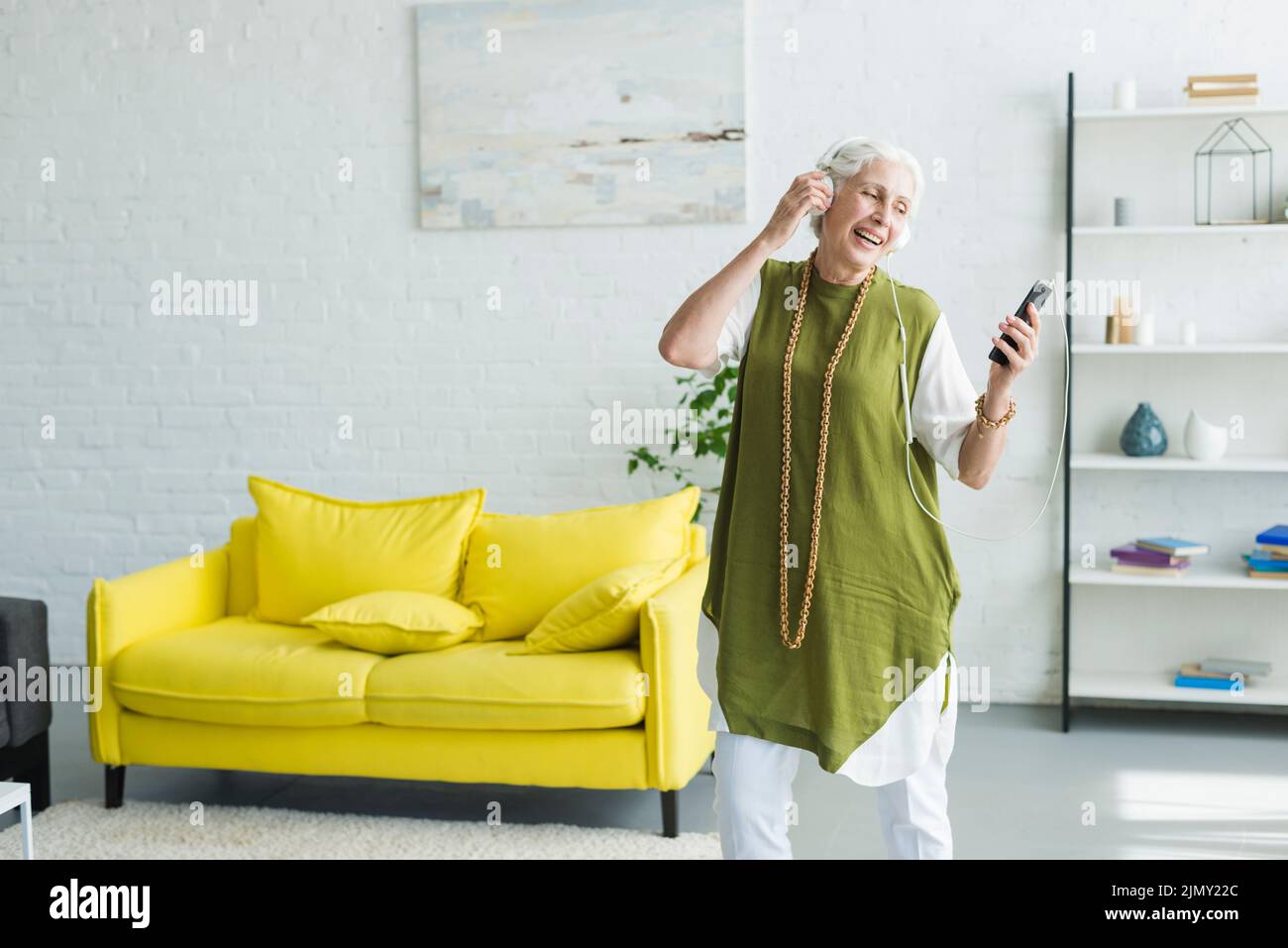Smiling senior woman listening music headphone through cellphone Stock Photo