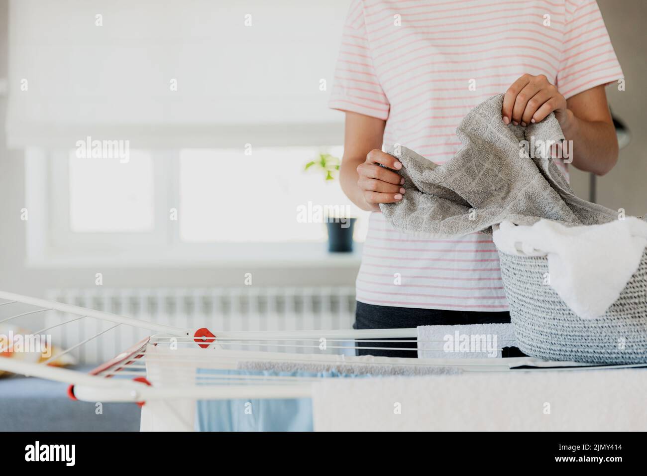 Woman hanging clean wet clothes laundry on drying rack at home in room