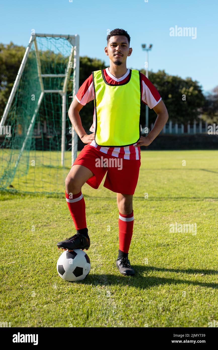 Portrait of young male player with arms akimbo and leg on ball over grassy field in playground Stock Photo