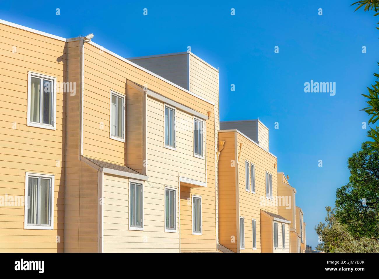 Apartment building exterior with yellow wood lap siding in San Francisco, California. Side view of an apartment building across the trees with casemen Stock Photo
