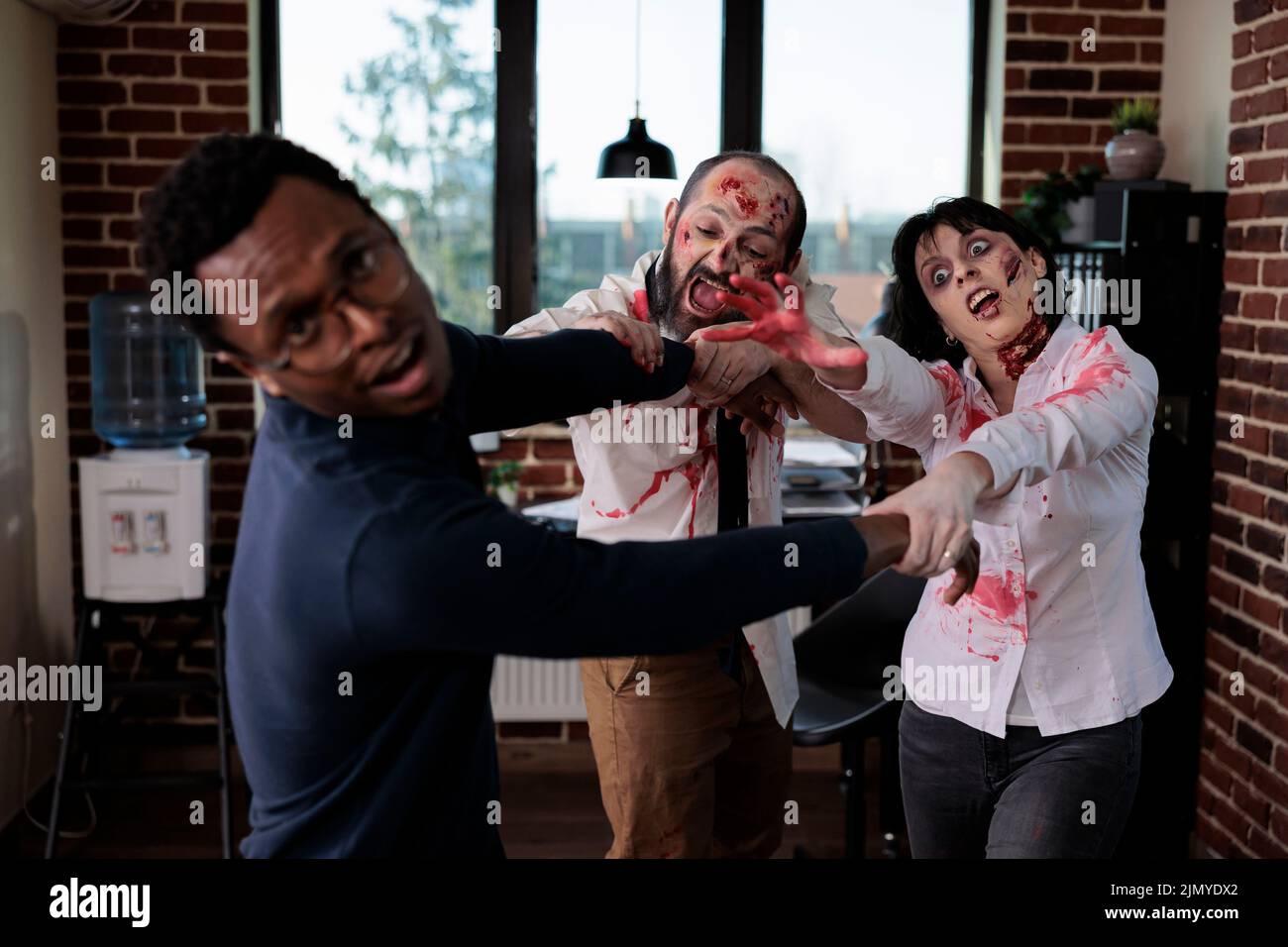 Cruel spooky zombies chasing after businessman, frightened person running from brain eating bloodthirsty monsters. Scared man being afraid of undead aggressive corpses, walking dead. Stock Photo