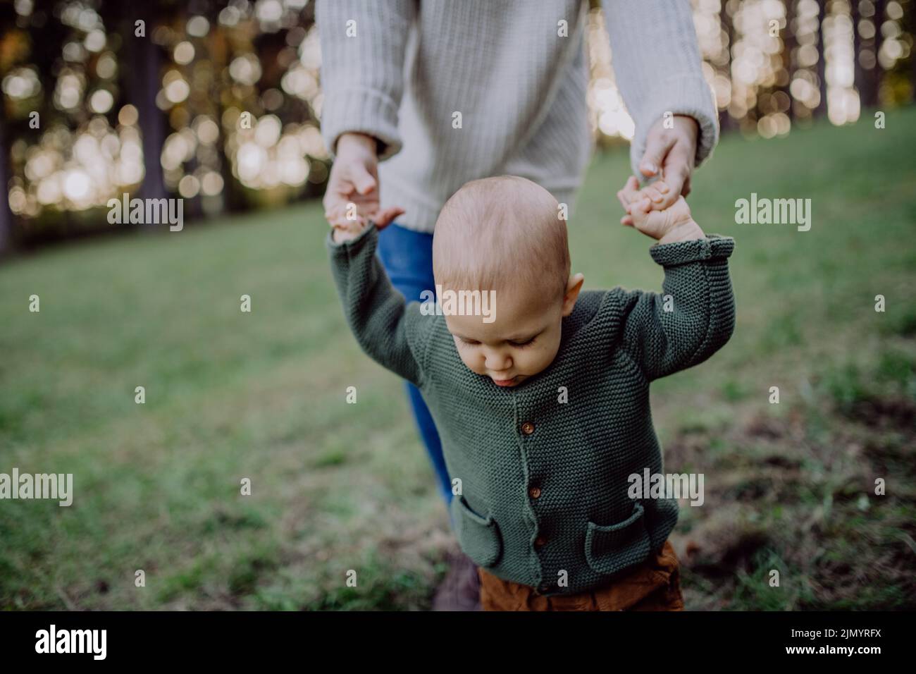 Mother holding hands of her baby son when walking in nature, baby's first steps concept. Stock Photo