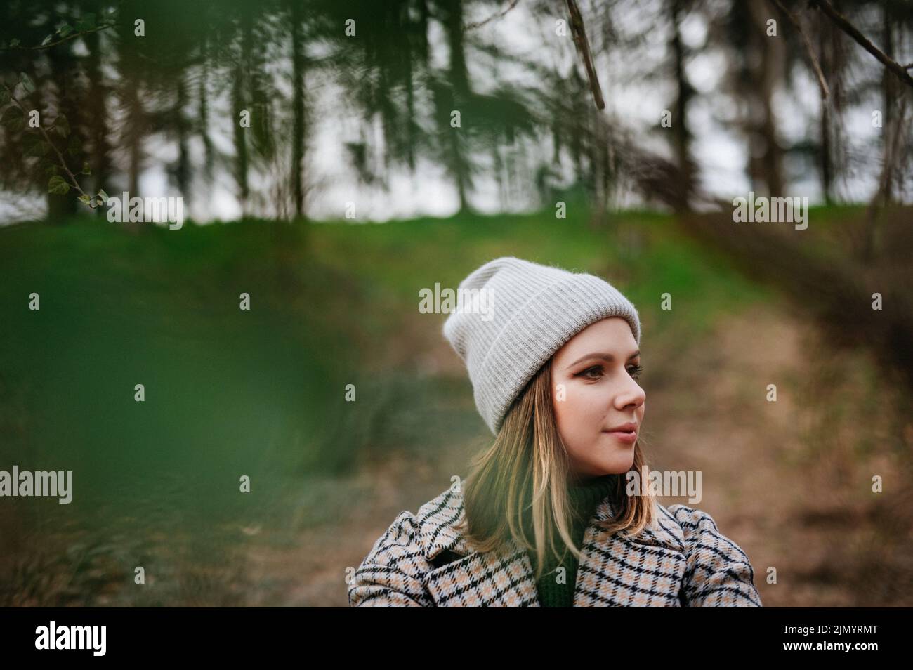Portrait of young woman in coat and knitted cap in autumn nature, walking in forest. Stock Photo