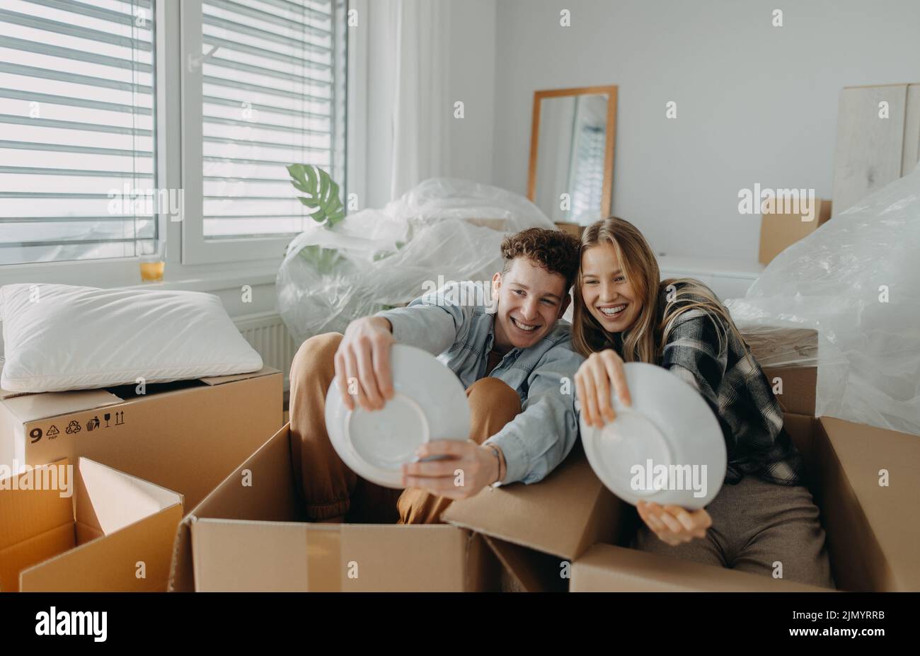 Cheerful young couple in their new apartment, having fun when unpacking. Conception of moving. Stock Photo