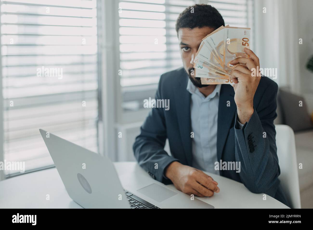 Depressed businessman man counting euro money working on computer at office desk and looking at camera, inflation concept. Stock Photo