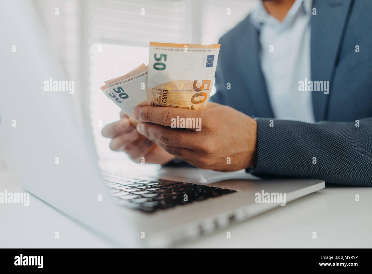 Businessman man with euro money in his hands is working on a computer keyboard at office desk, close-up Stock Photo