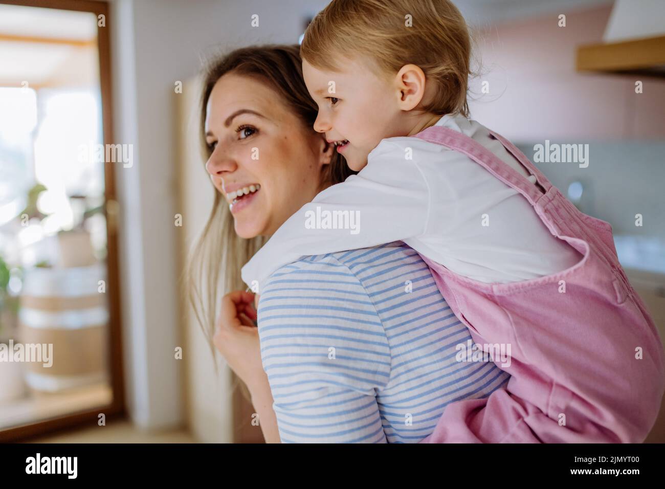 Young mother giving piggy back ride to her little daughter. Stock Photo