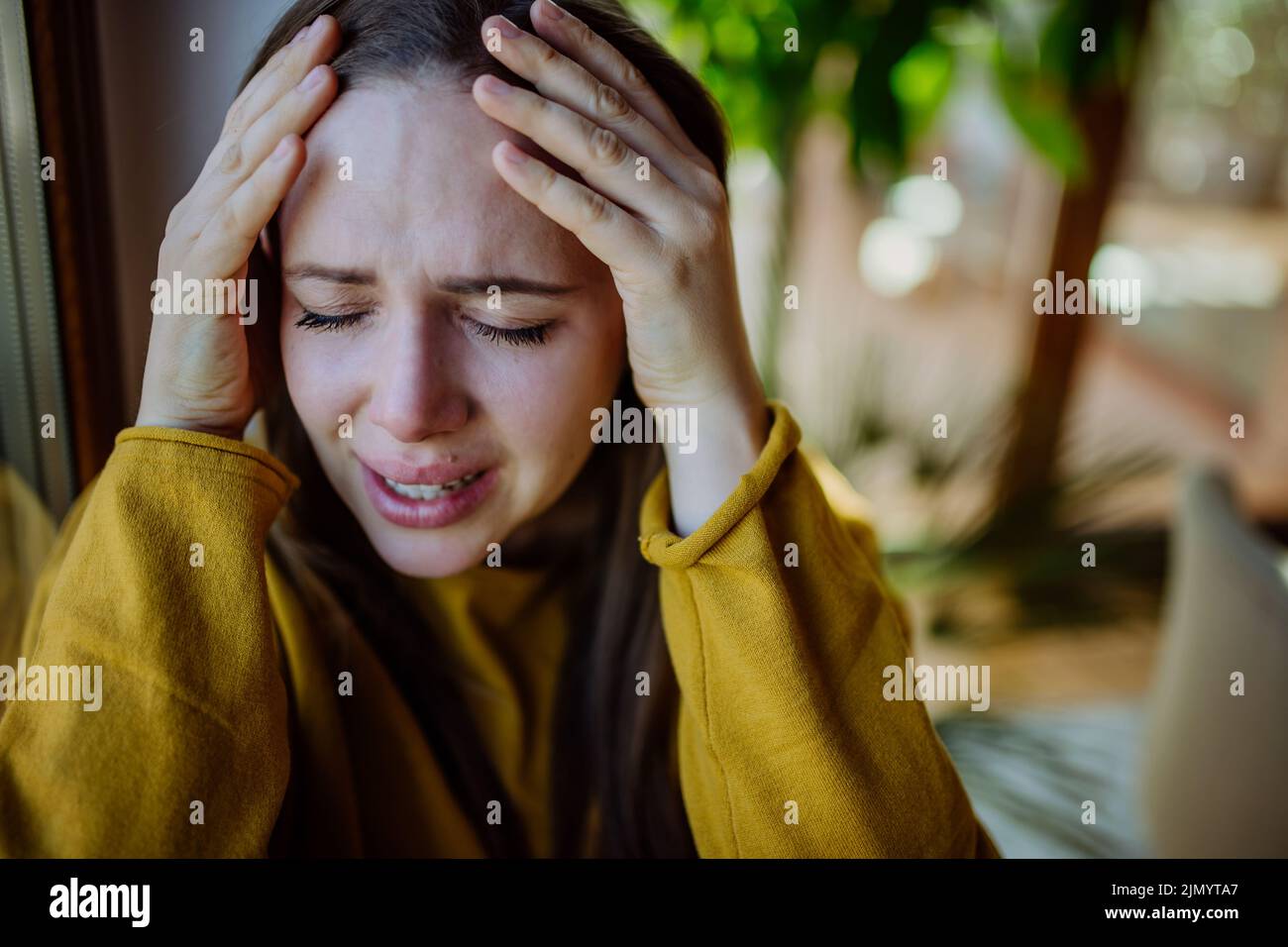 Woman suffering from depression and crying at home, holding head in her hands. Stock Photo