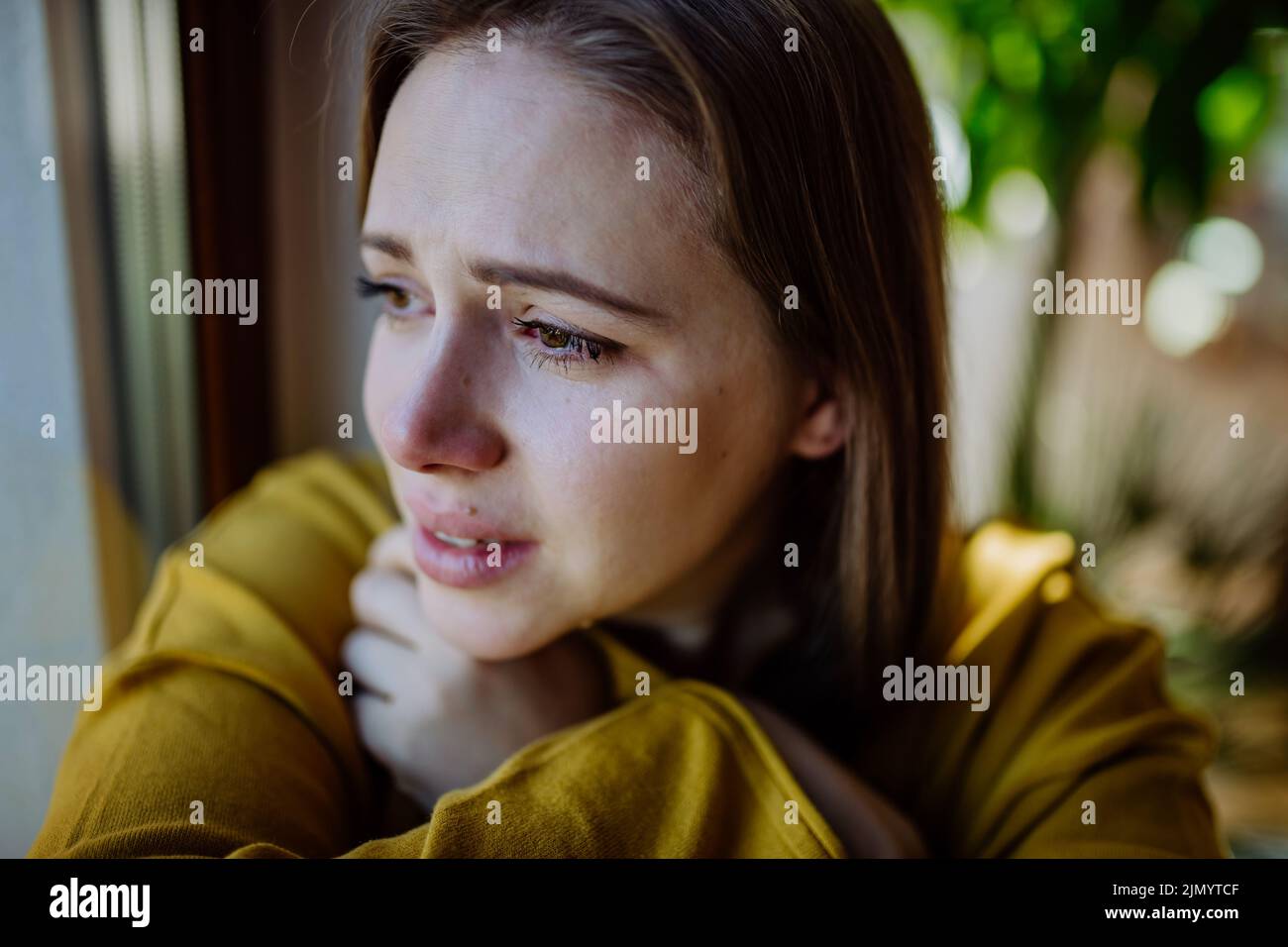 Woman suffering from depression at home, crying and looking trough the window. Stock Photo