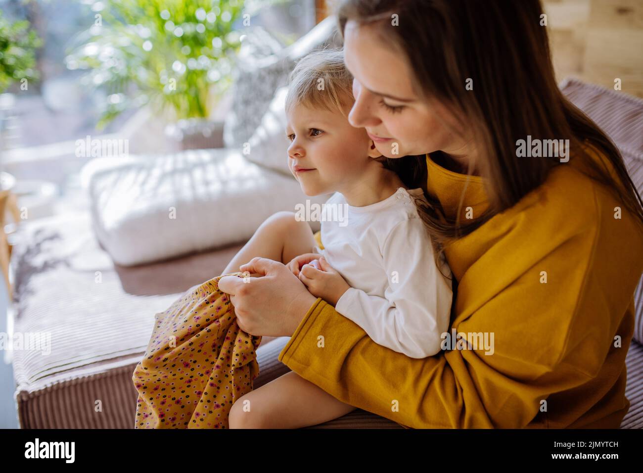 Young mother dressing up her little daughter in their home, moterhood concept. Stock Photo