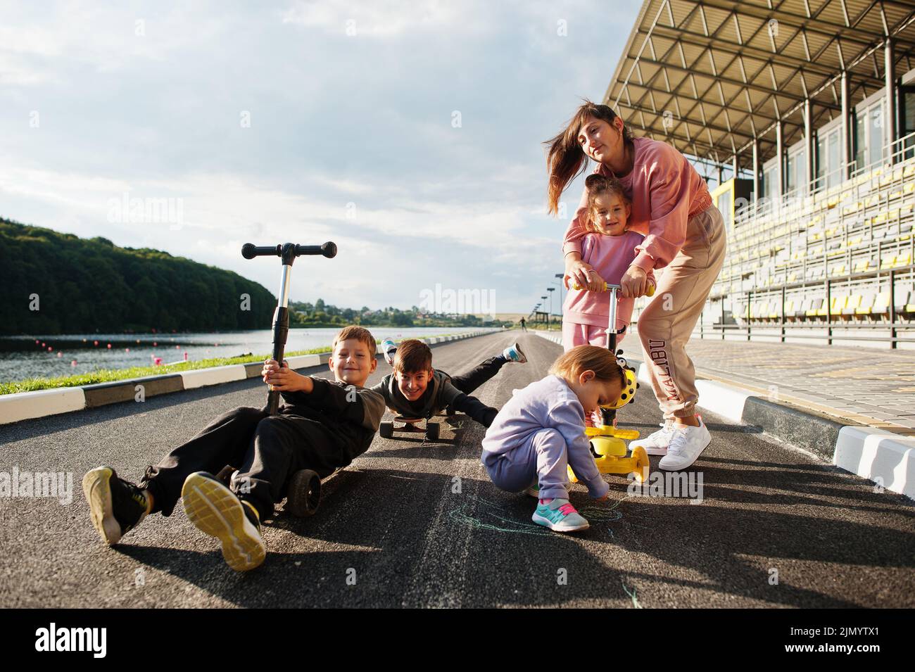 Kids Using Scooters Young stylish mother with four kids outdoor. Sports family spend free ...