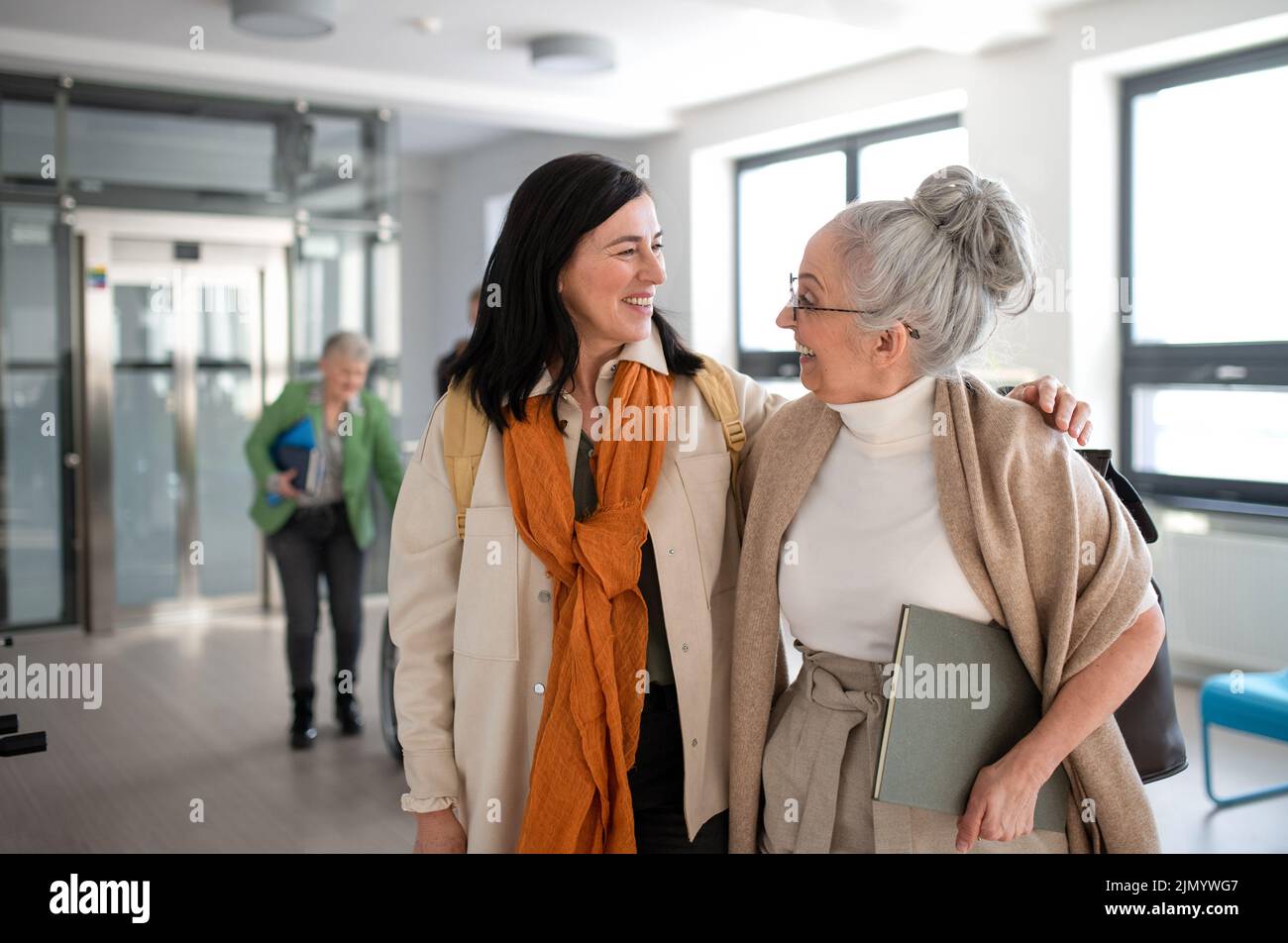 Happy mature woman student with book discussing with teacher in corridor in university. Stock Photo
