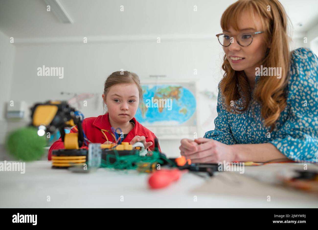 Down syndrome schoolgirl learning about robotics of teacher during class at school, integration concept. Stock Photo