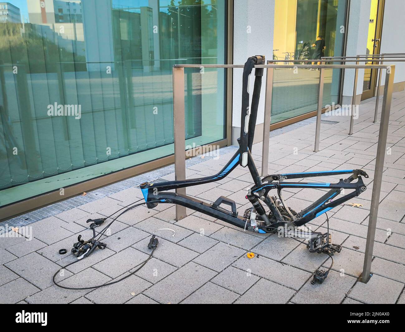 Only the frame of a black and blue valuable high end mountain bike chained to bicycle stand is left, all other  components have been taken off and sto Stock Photo