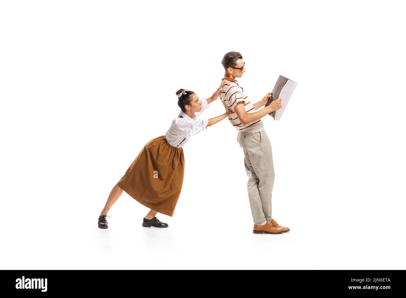 Portrait of young woman pushing man reading newspaper isolated over white background. Retro style Stock Photo