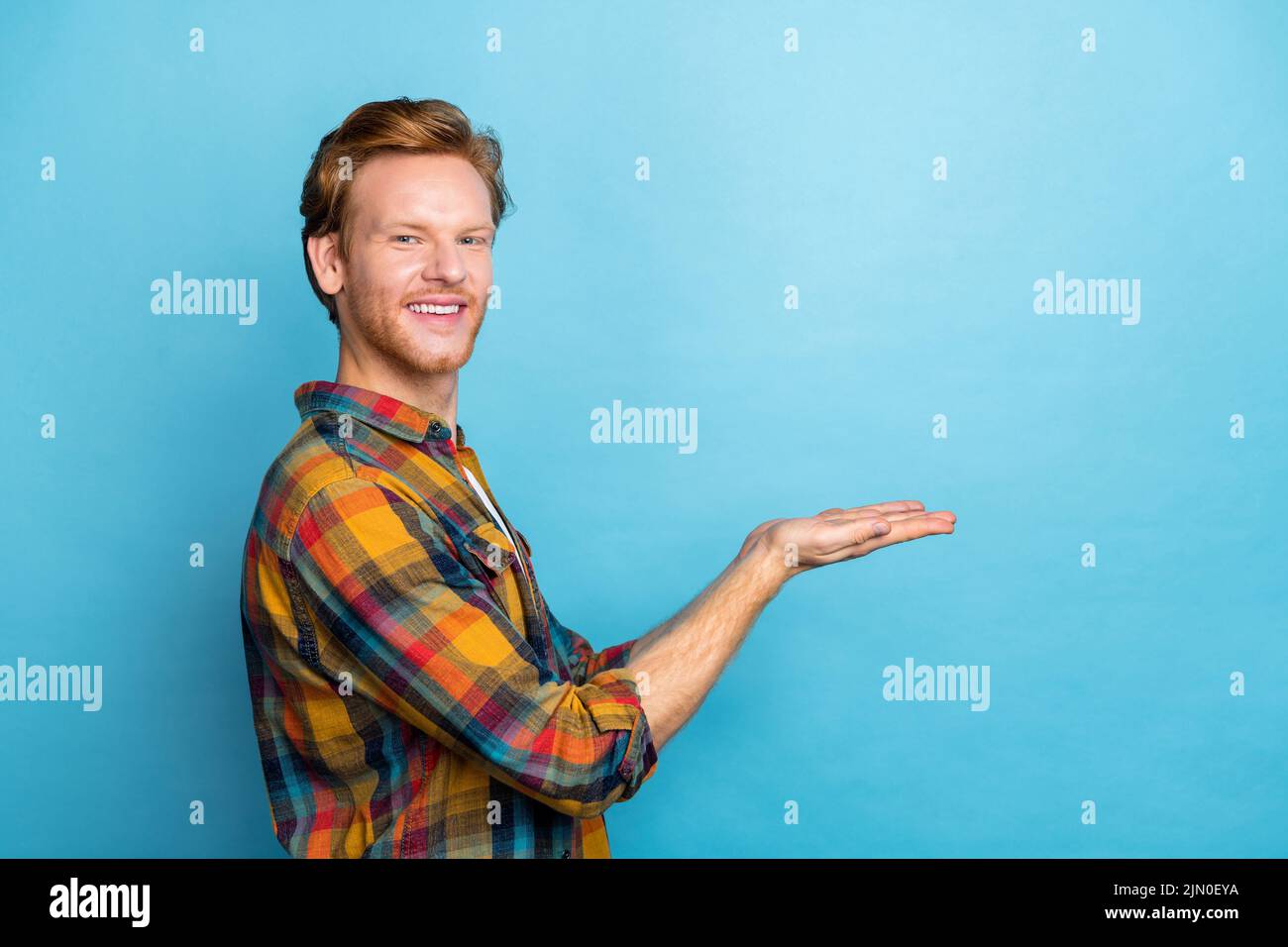 Photo of handsome positive stylish guy with ginger hair dressed plaid shirt showing at empty space isolated on blue color background Stock Photo