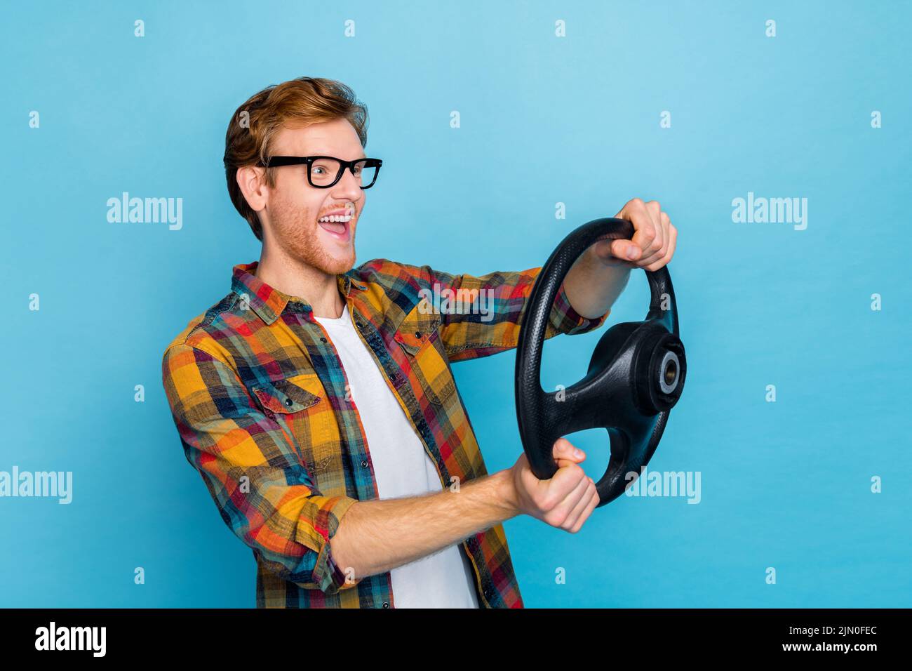 Photo of cheerful handsome guy dressed plaid shirt glasses hold steering wheel say yes look empty space isolated on blue color background Stock Photo