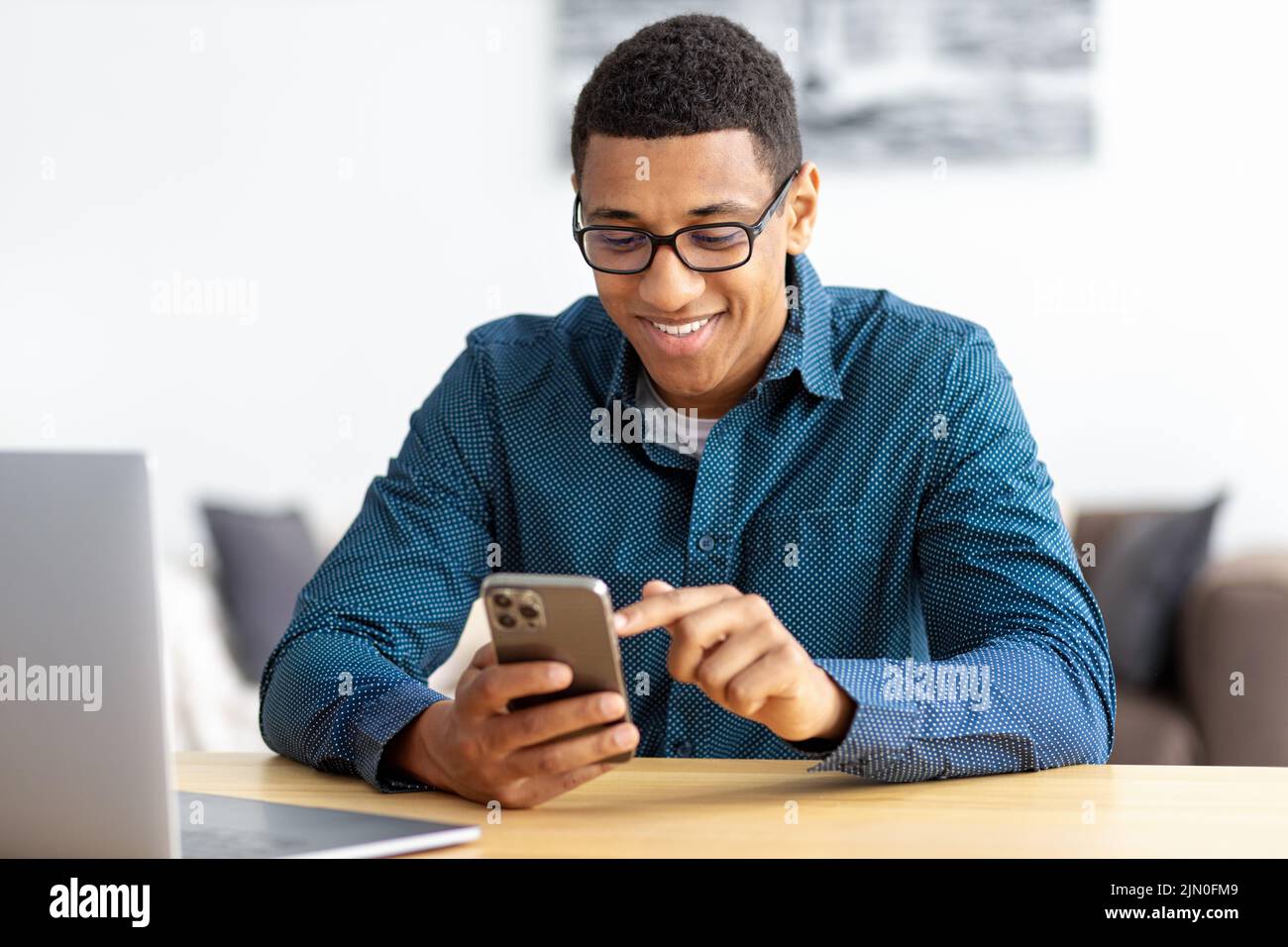 African American man entrepreneur in modern office looking at screen typing message with mobile phone Stock Photo