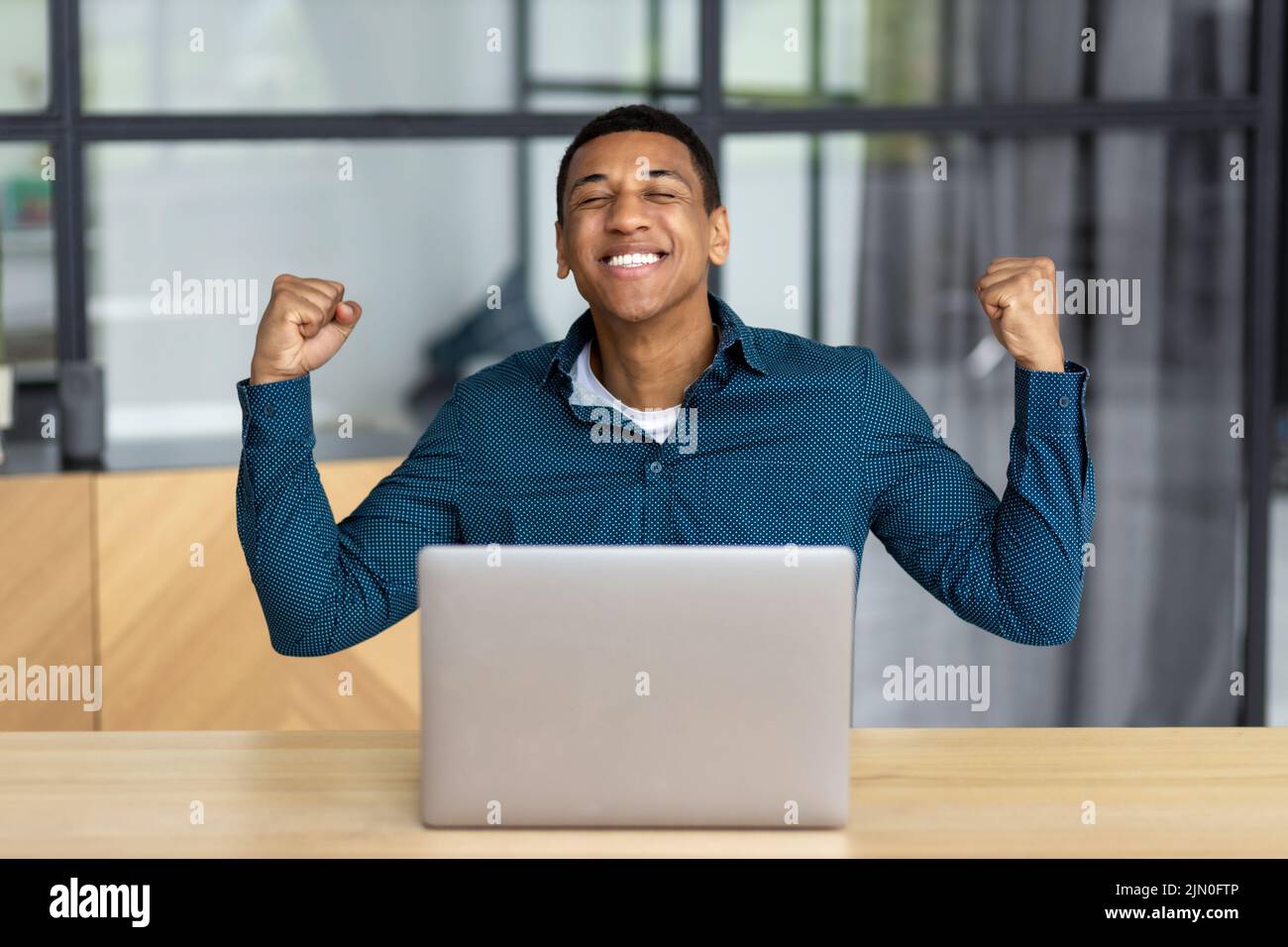 Excited young man celebrating success while sitting with laptop workplace Happy businessperson male having good news Stock Photo