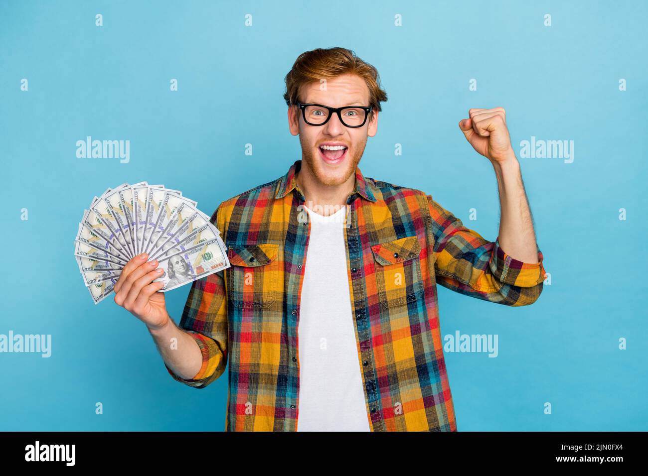 Photo of astonished handsome lucky man with ginger hair wear checkered shirt finally win handreds of dollars isolated on blue color background Stock Photo