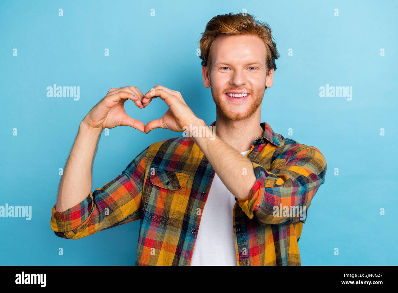 Photo of handsome cheerful satisfied man with ginger hairstyle dressed plaid shirt showing heart gesture isolated on blue color background Stock Photo