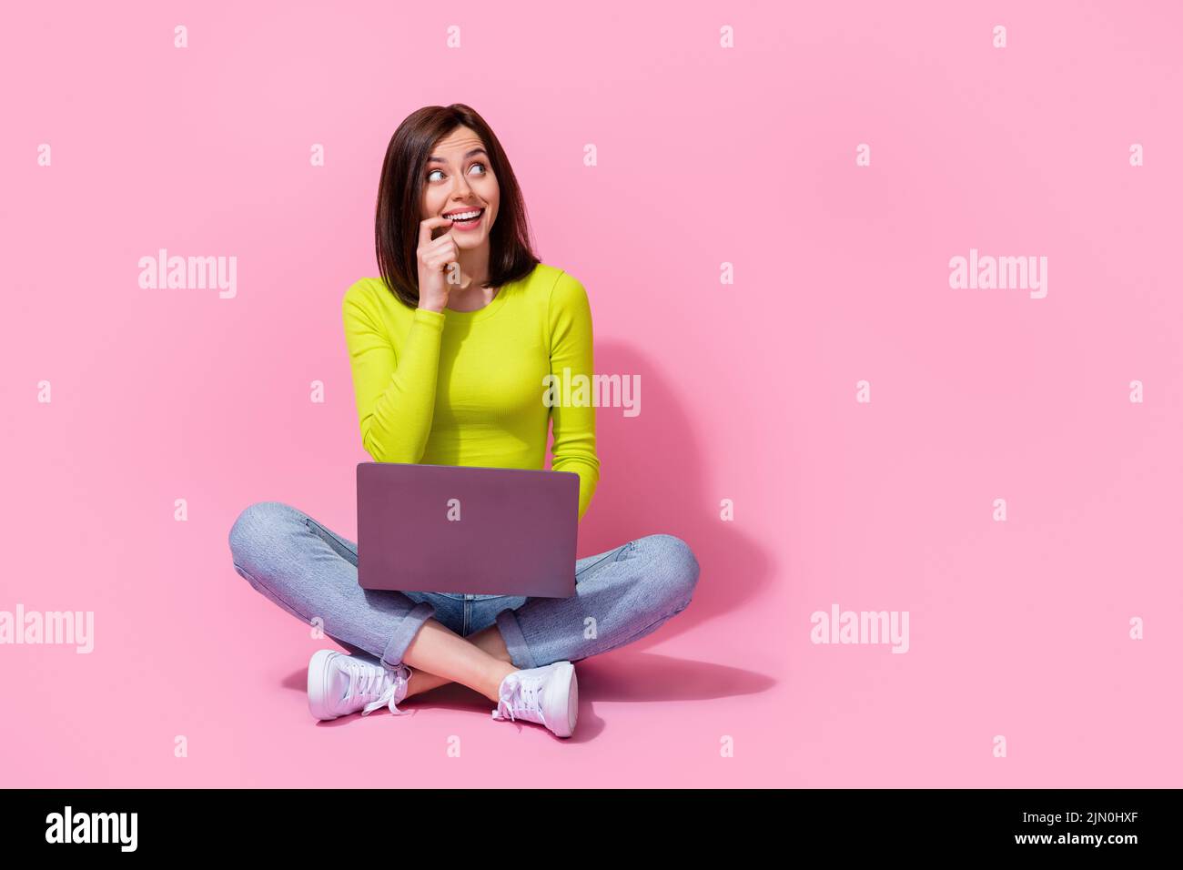 Photo of cunning positive playful lady sit look up blank space use gadget device have plan idea hmm isolated on pink color background Stock Photo
