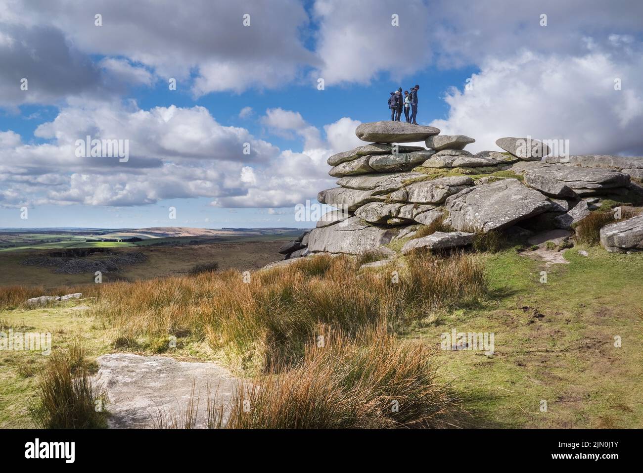 A group of walkers standing on the top of a rock stack left after glacial action on the summit of Stowes Hill on Bodmin Moor in Cornwall. Stock Photo
