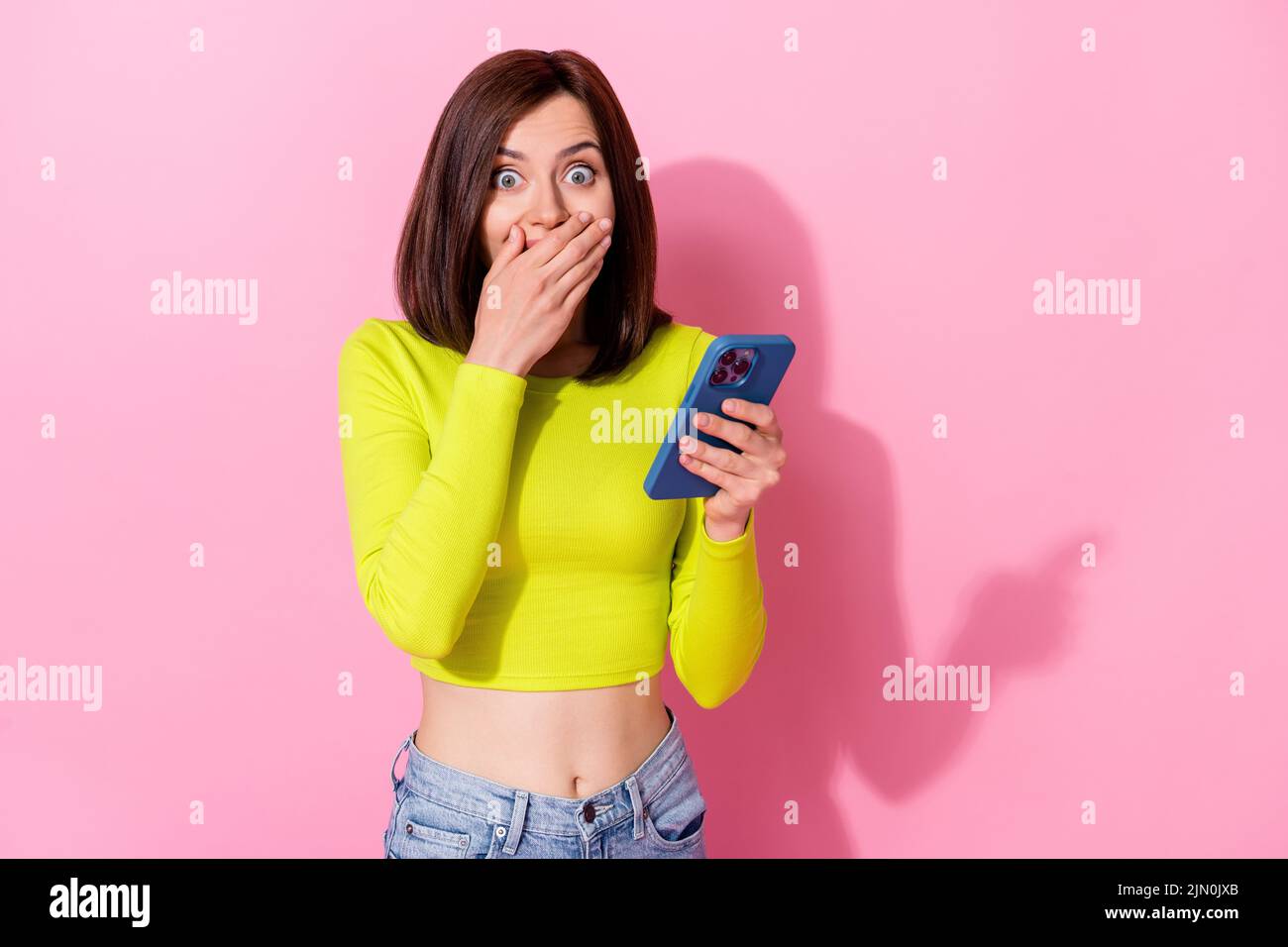 Photo of pretty shocked lady wear yellow top arm cover lips reading modern gadget empty space isolated pink color background Stock Photo