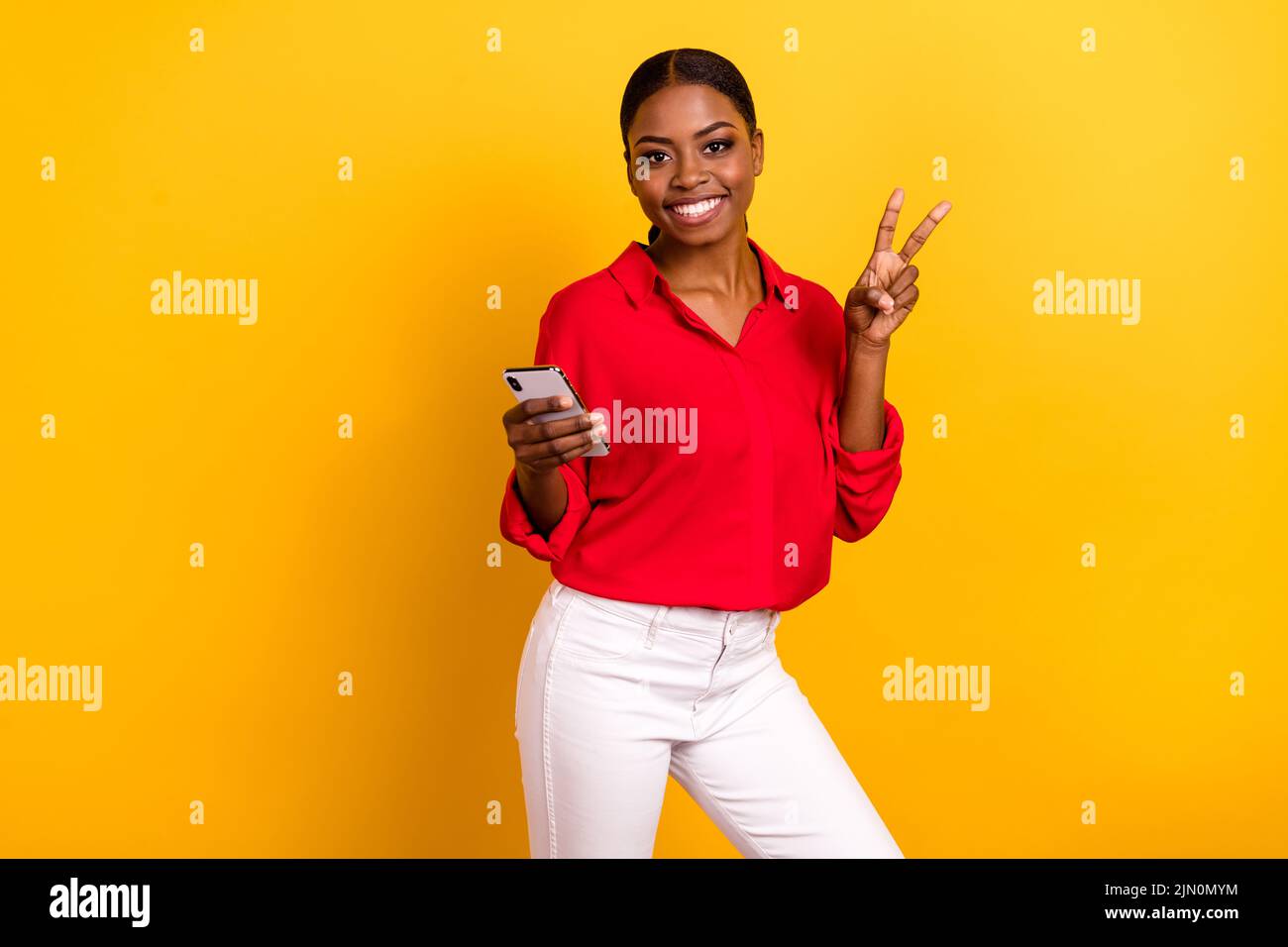Photo of young cheerful girl show fingers peace v-symbol use mobile influencer isolated over yellow color background Stock Photo