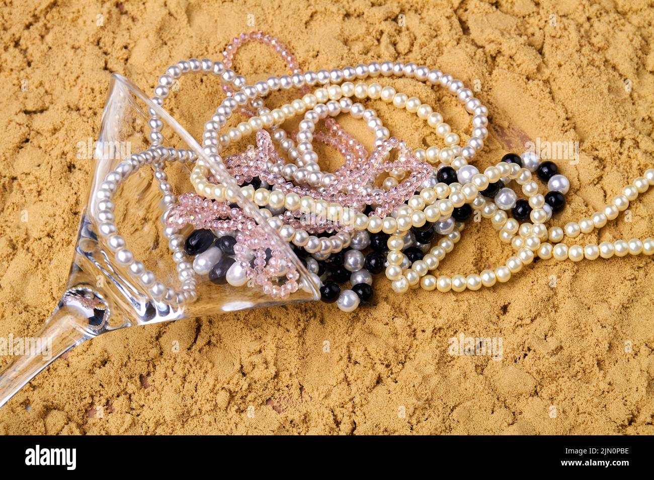 Cocktail glass with pearl necklaces on the sand. Accessories on the beach. Stock Photo