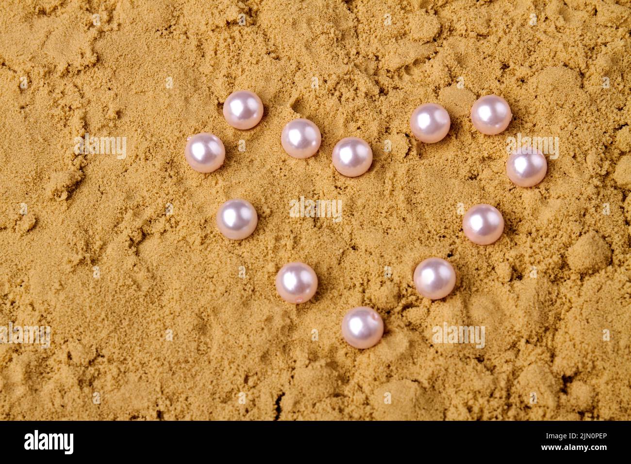 Close up pearls in the shape of heart. Wet sand and copy space. Stock Photo