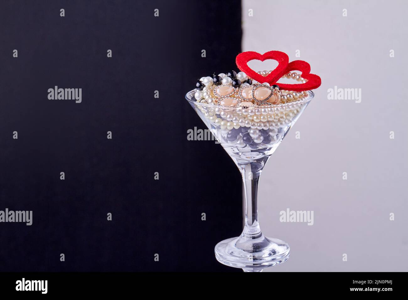 Cocktail glass with jewelry and hearts. Black and white background. Stock Photo
