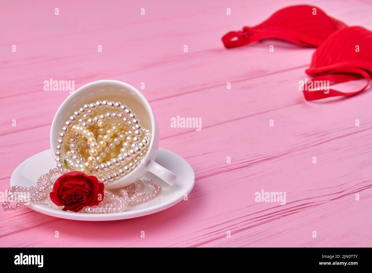 White teacup full of pearl necklaces with red flower. Pink wooden desk. Stock Photo