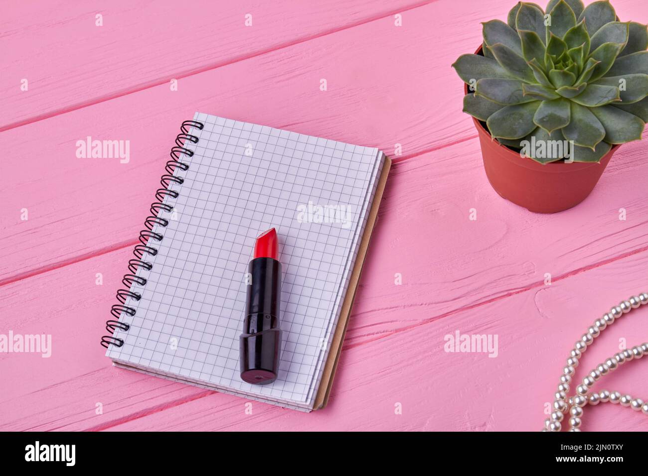 Top view notepad with lipstick on pink wooden desk. Notebook with copy space. Stock Photo