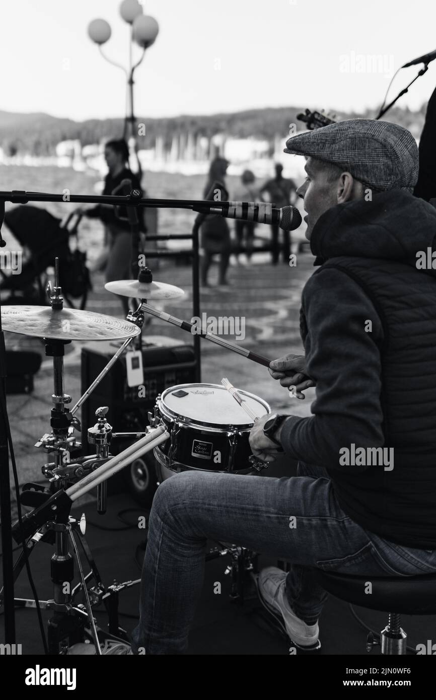 A vertical grayscale shot of a male singing and playing on drums on a street in Velden am Worthersee, Austria Stock Photo